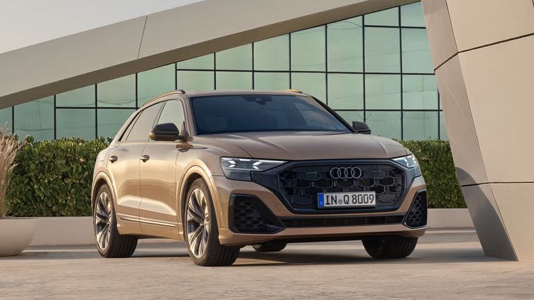 Der Q8 SUV schräg von vorn parkt vor einem modernen Gebäude. Eine bepflanzte Hecke trennt das Fahrzeug von dem dahinter liegenden, voll verglasten Gebäude.